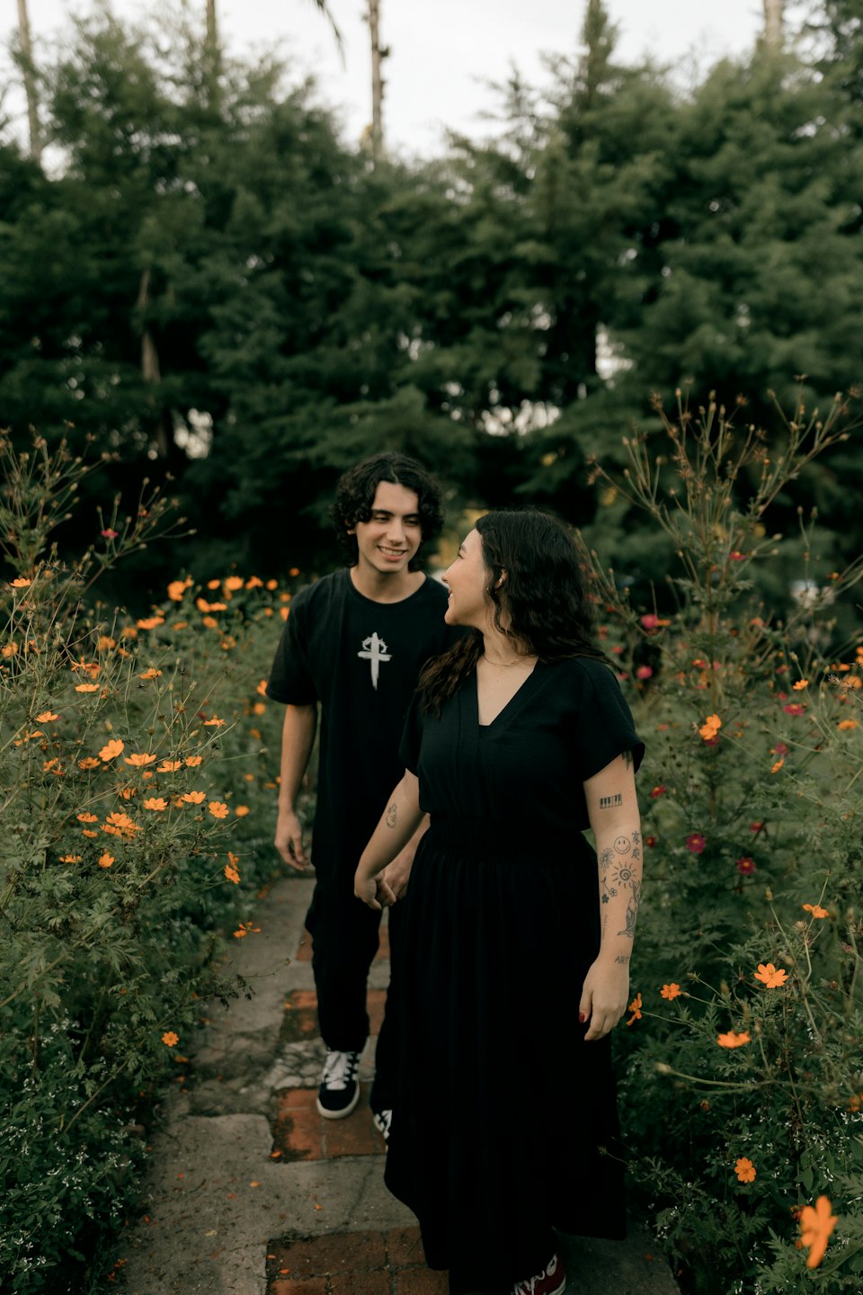 A couple holds hands while walking through a flower garden.