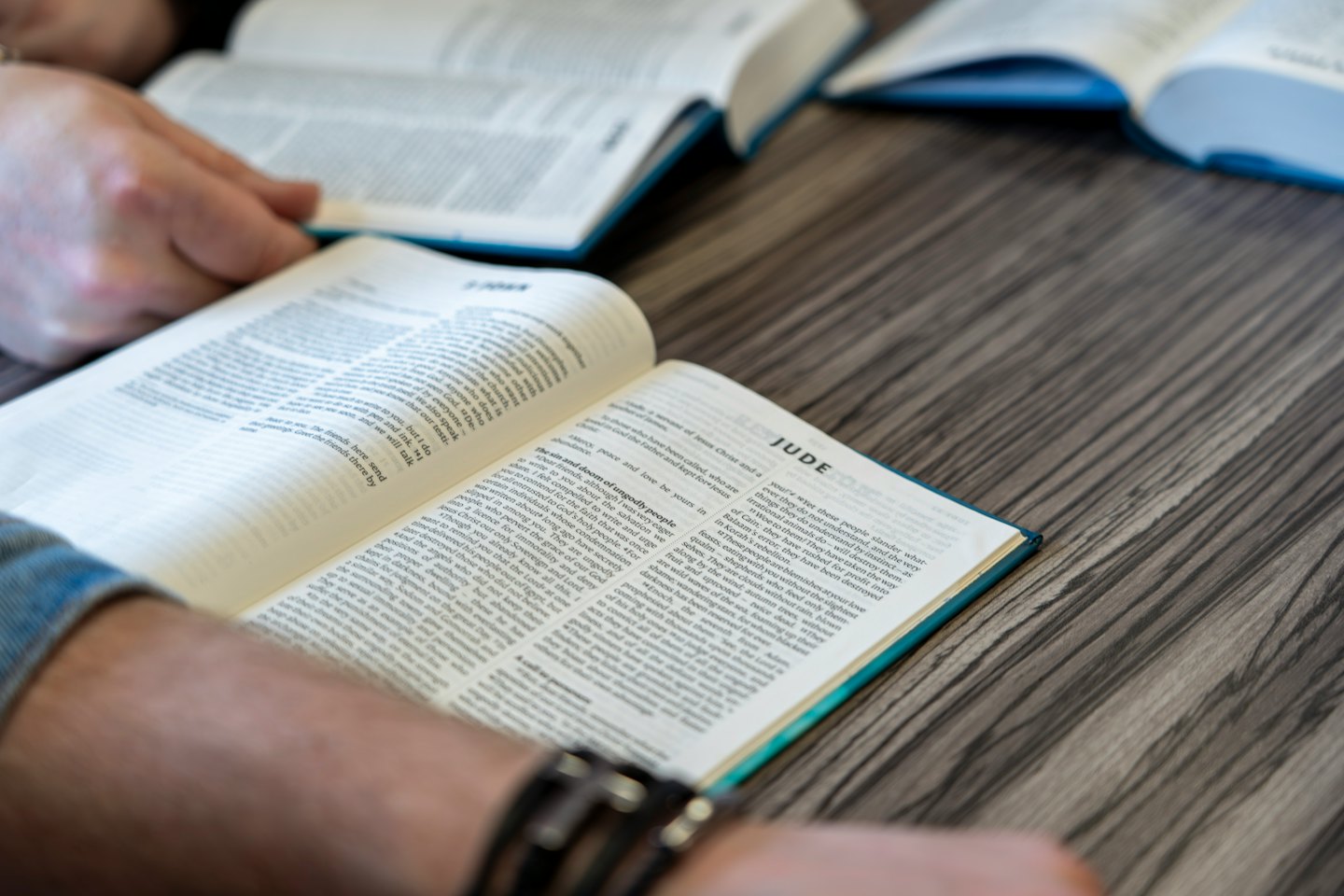 Two people read from open books on a wooden table.