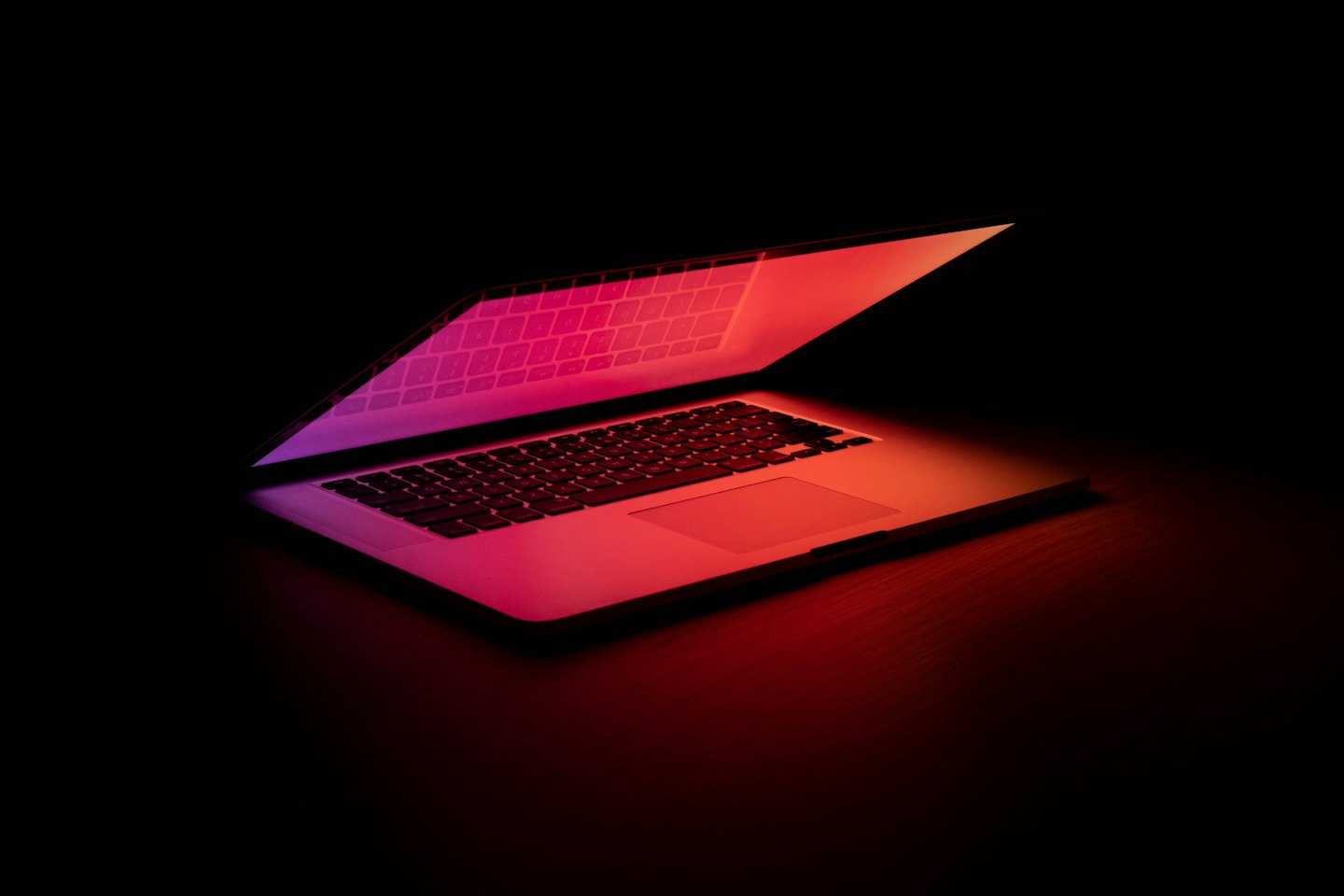 A modern laptop reflects its keyboard on a dark surface.