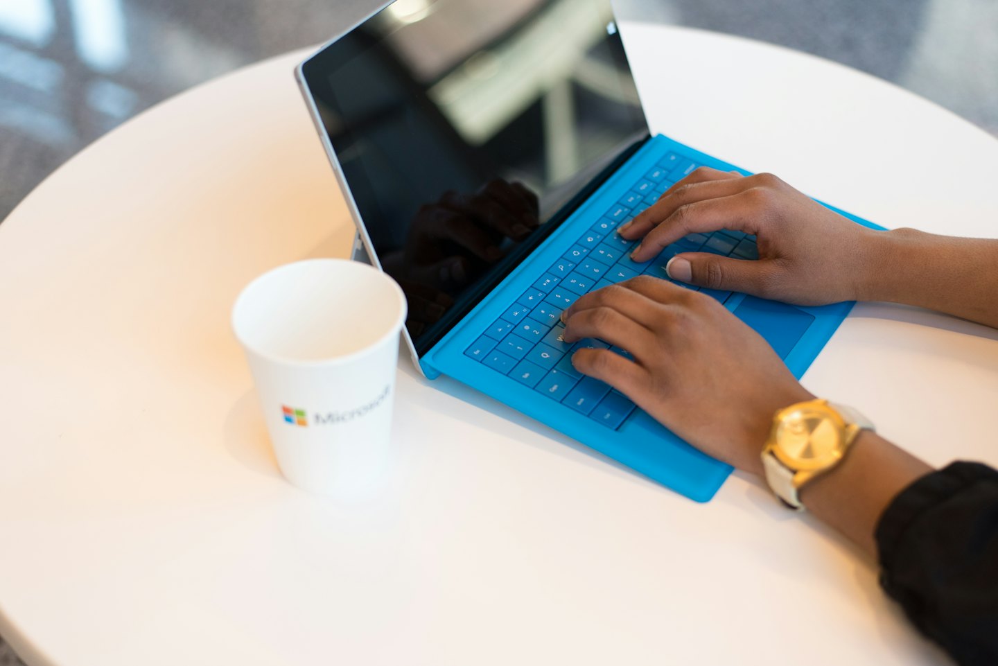 Hands typing on a blue laptop at a round table.
