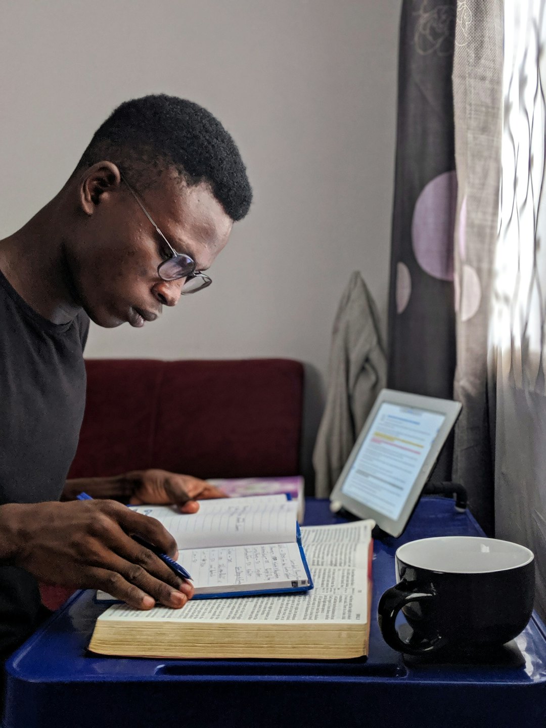 Young man studying from a book and tablet at a table.