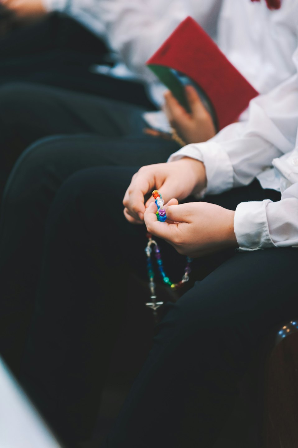Hands holding a colorful beaded rosary with a silver crucifix.