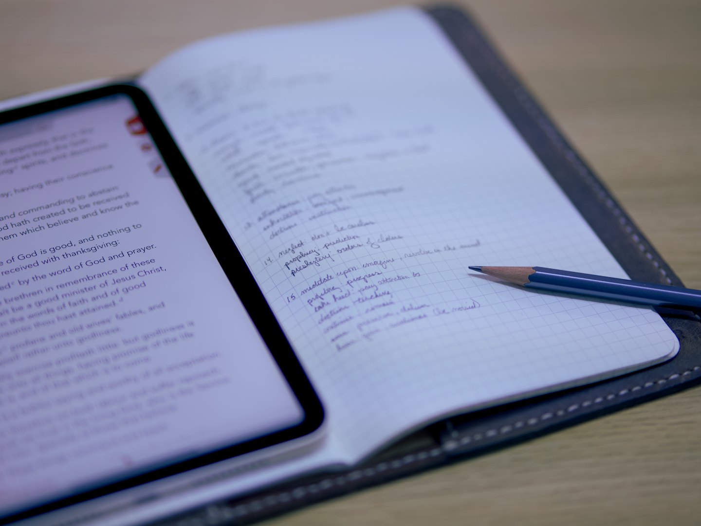 Digital tablet and notebook with handwritten notes on wooden desk.