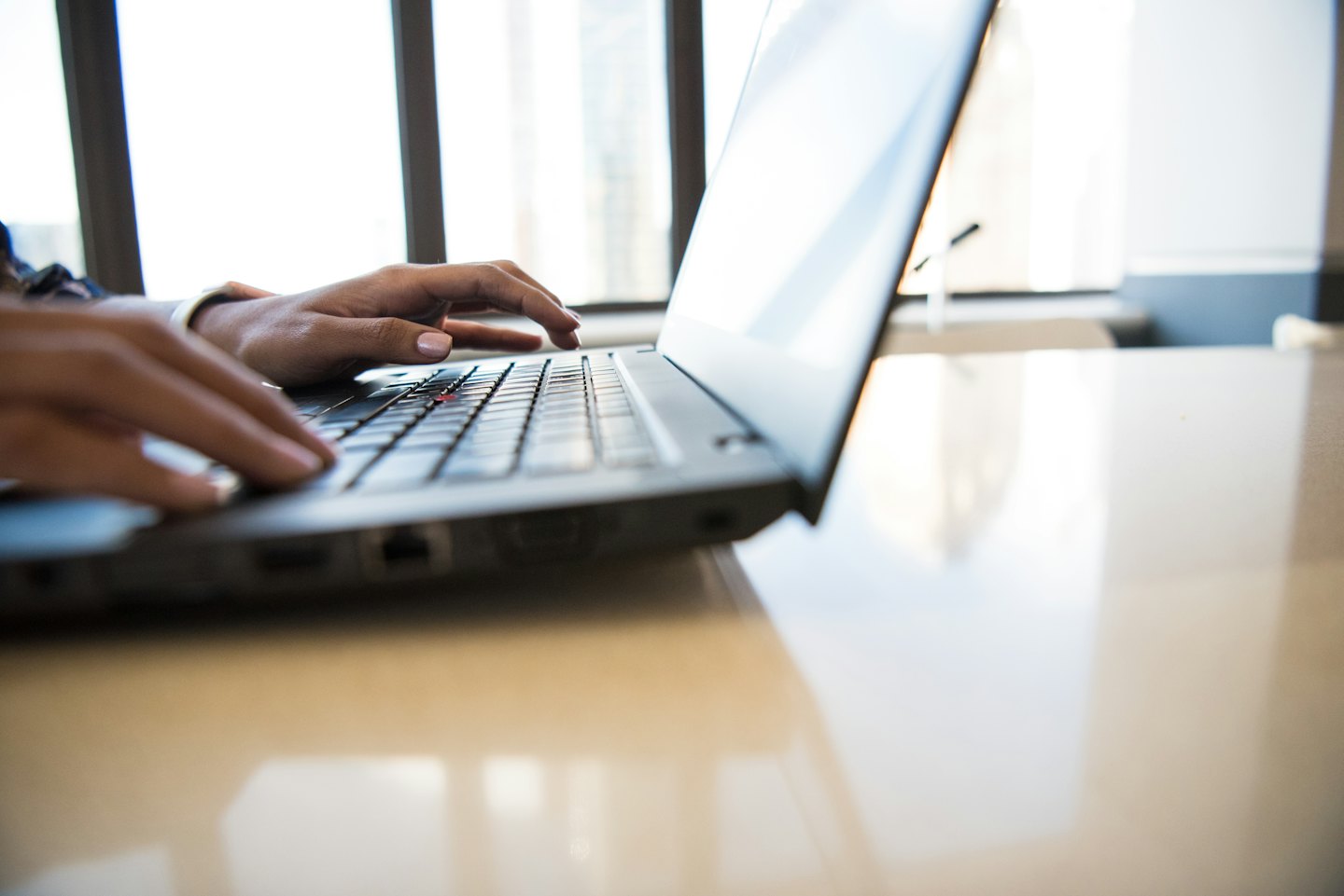 Dark-skinned hands typing on a laptop keyboard.