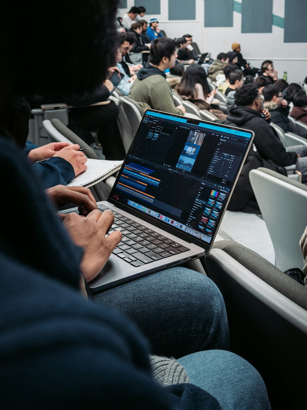 Hands editing video on a laptop in a lecture hall.