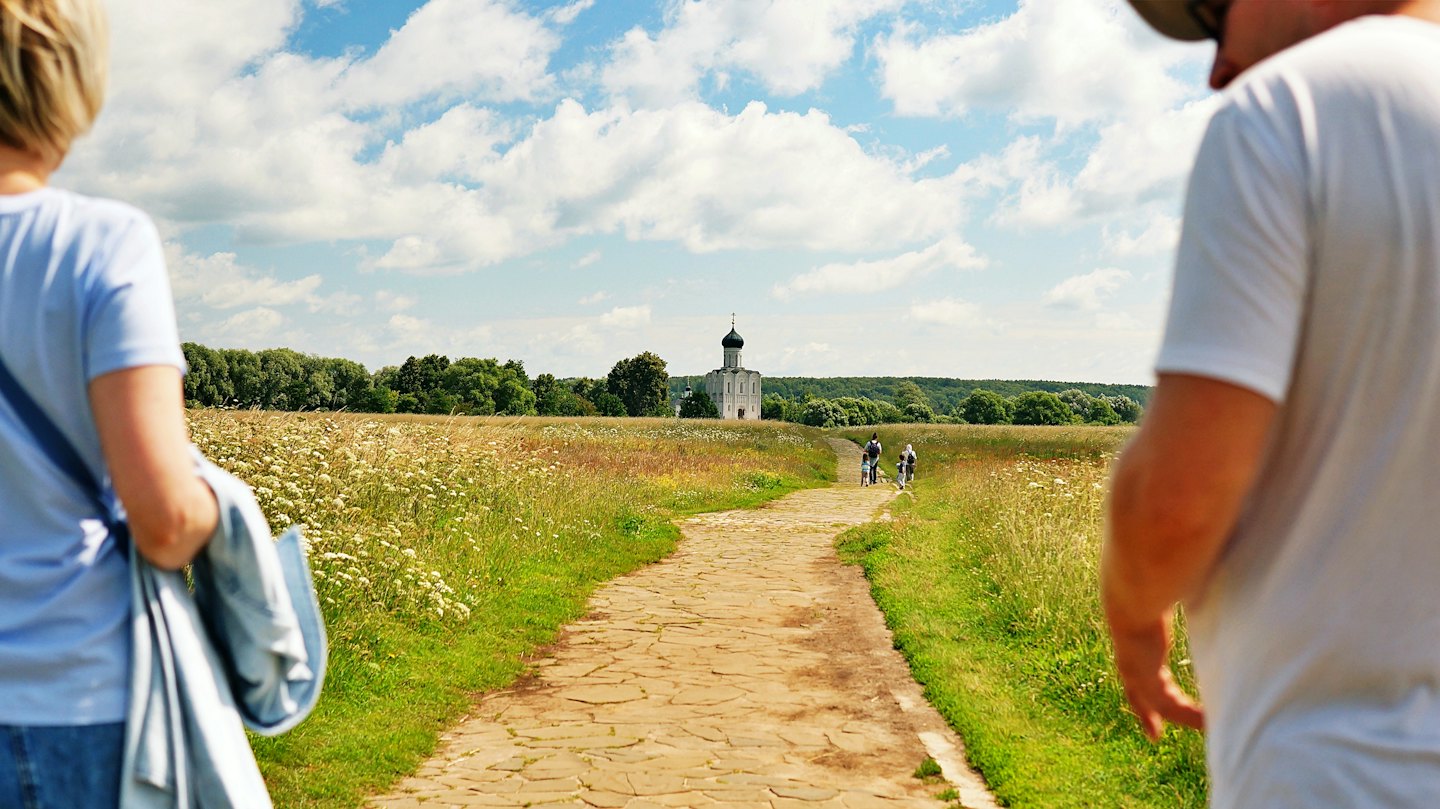 Two people walk along a path toward a distant church.