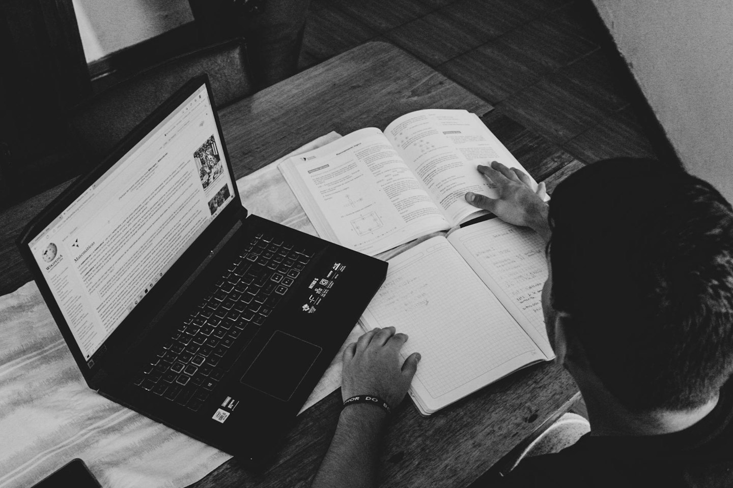 Student studying at a wooden desk with a laptop and textbook.