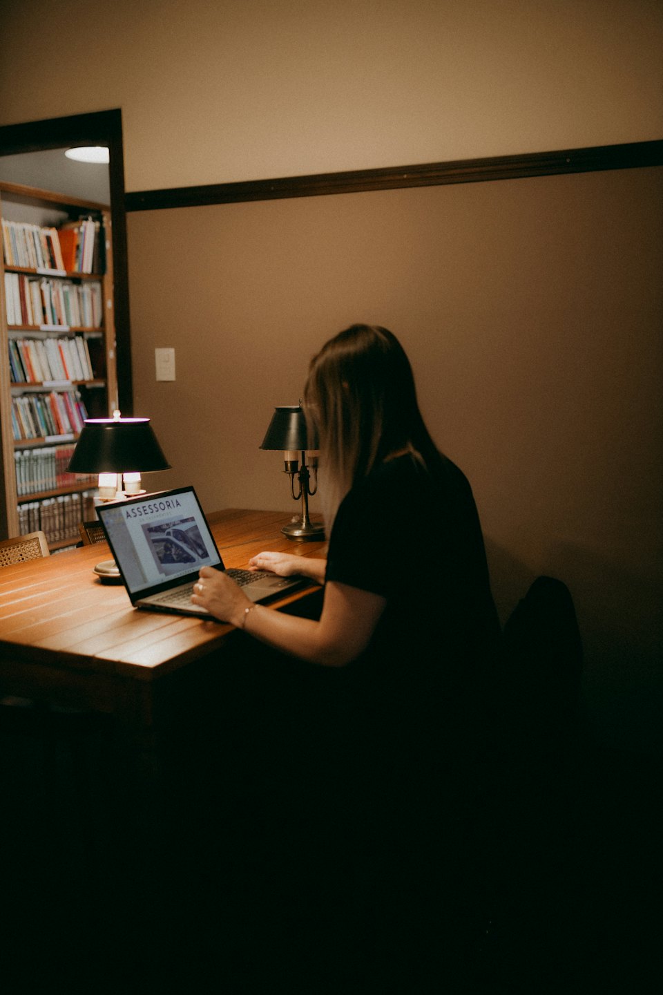 Person working on laptop at wooden desk with lamps.